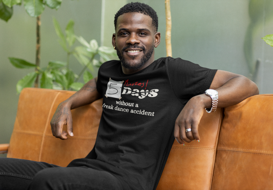 Male wearing a black dance tshirt design with the text "5 days without a freak dance accident" where the word "days" is crossed over and "minutes" is written in red above it.