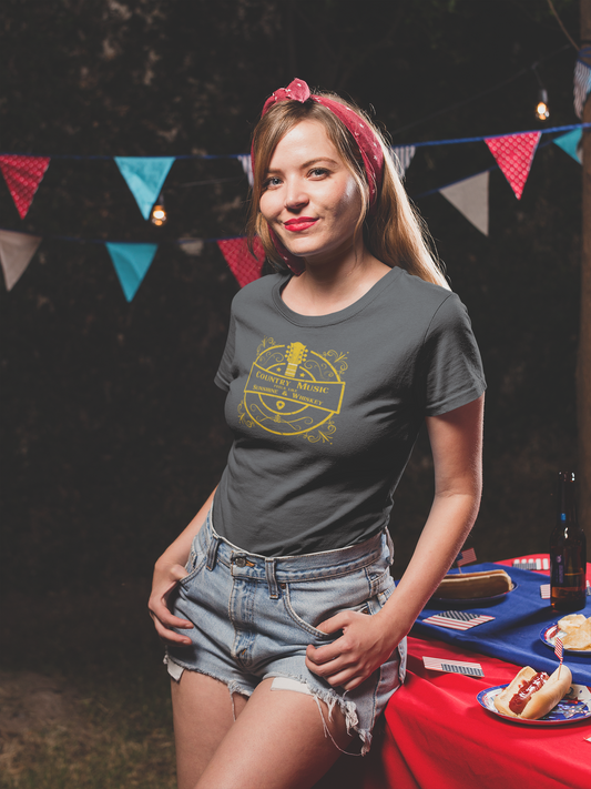A female wearing a grey country music tshirt design with the text "Country music feels like sunshine & whiskey". The images on it is a golden guitar surrounded by golden colored retro graphics