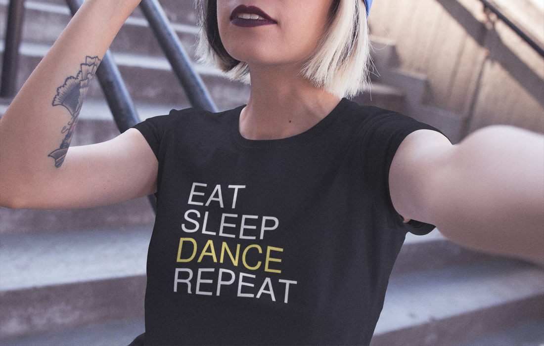 A woman taking a selfie while wearing a black dance tshirt design with the text "eat sleep dance repeat"