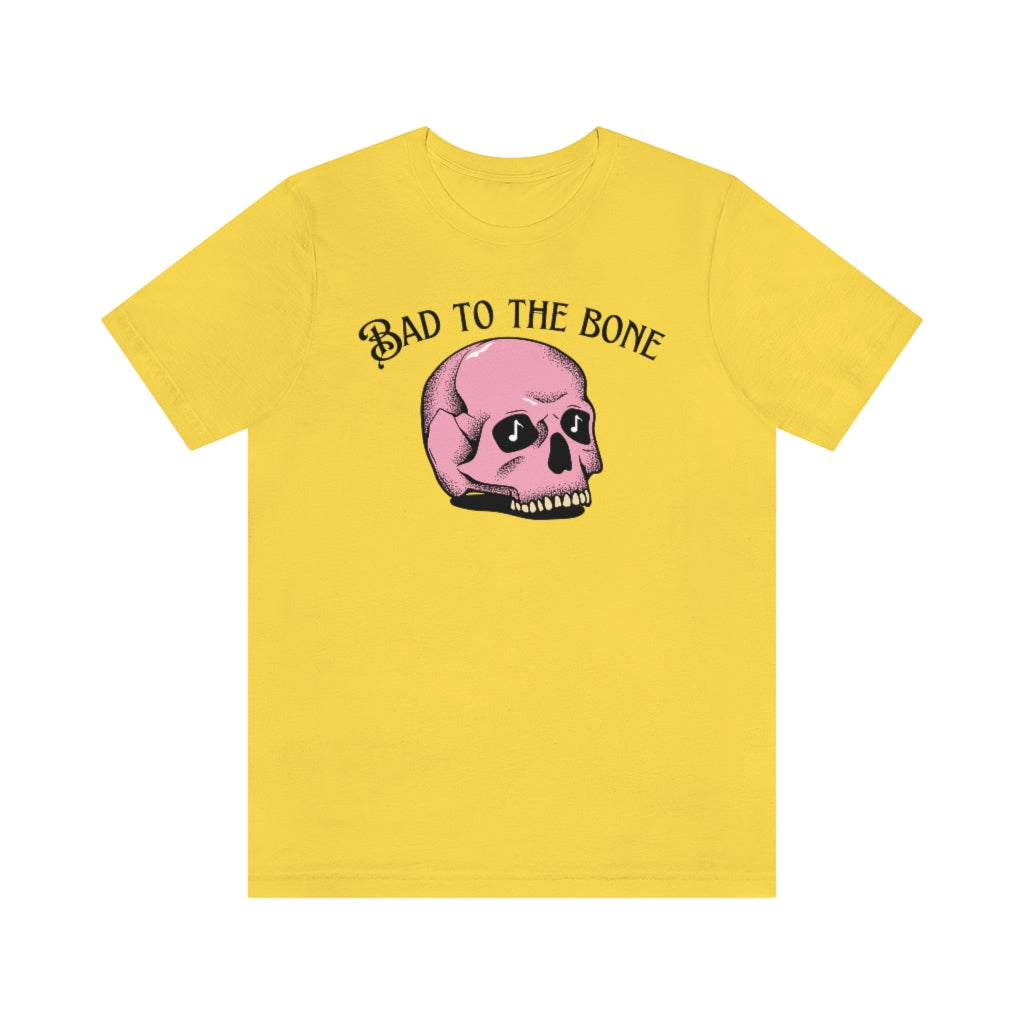 A yellow T-shirt with the text "bad to the bone" and a cartoony pink skull beneath it  having music notes in its eye sockets.