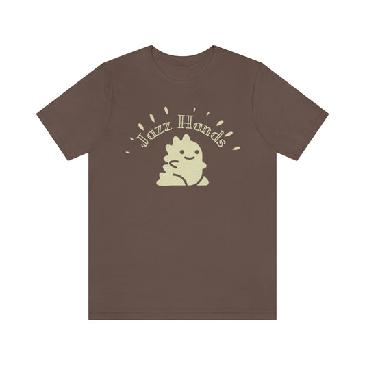 A brown T-shirt with an adorable dinosaur. It is waving its proportionally small hands and doing the most charming form of jazz hands. Above it is the text "Jazz Hands" in a very retro font. 